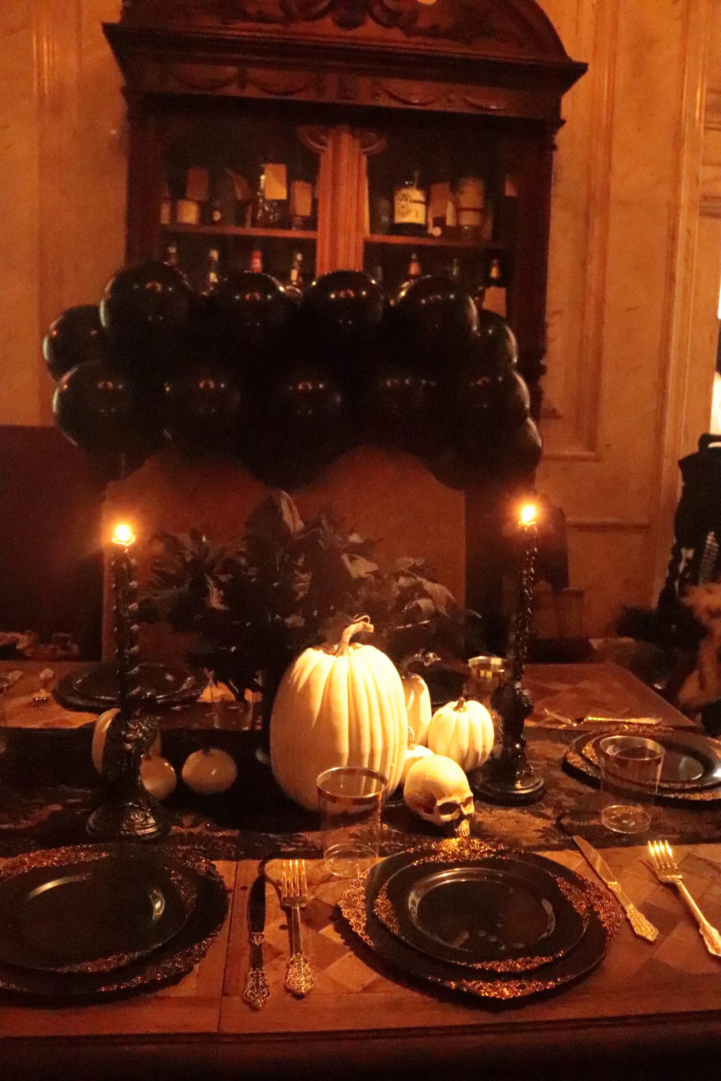 Black and gold Halloween party table with white pumpkins, skull decor, black candles, lace runner and black balloon backdrop