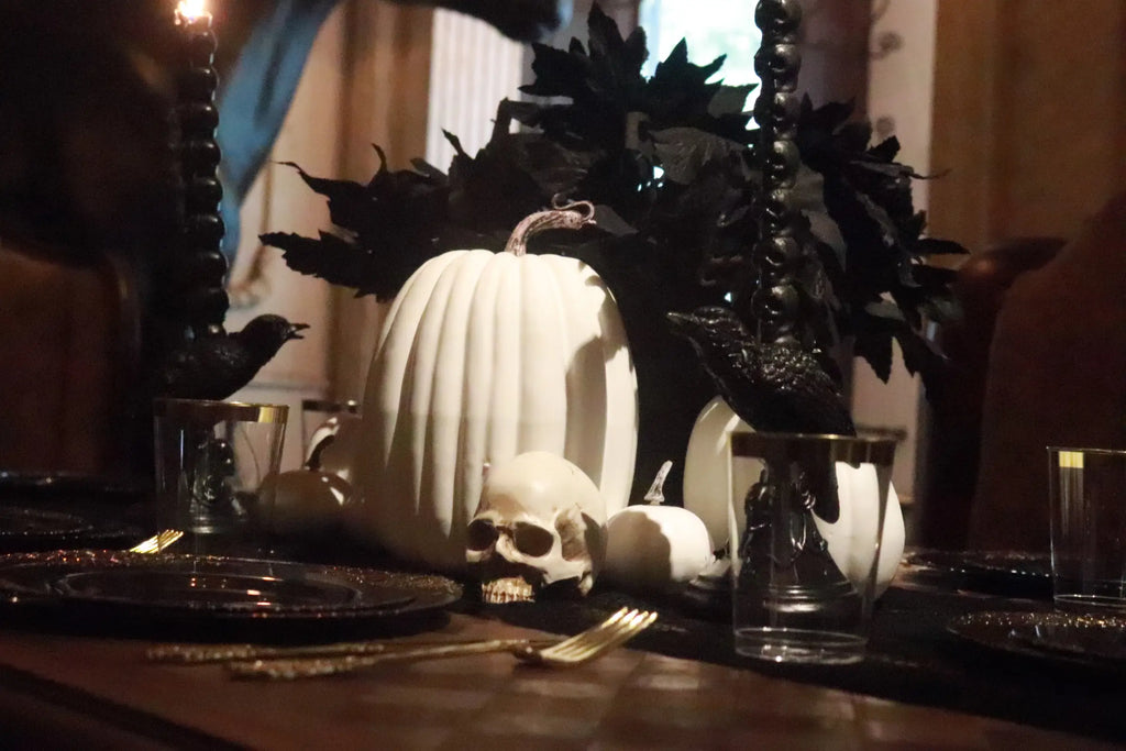 Gothic Halloween centerpiece with white pumpkins, skull, black leaves, black candles and elegant black and gold tableware