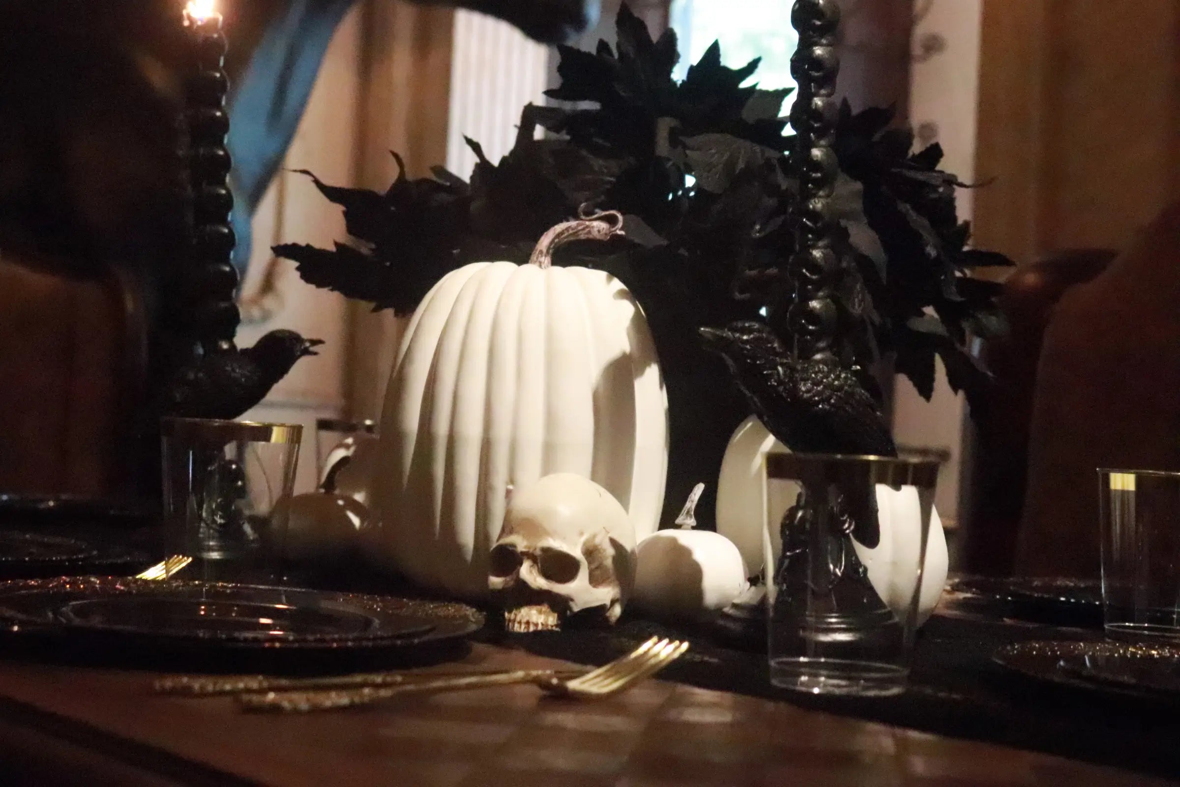 Gothic Halloween centerpiece with white pumpkins, skull, black leaves, black candles and elegant black and gold tableware