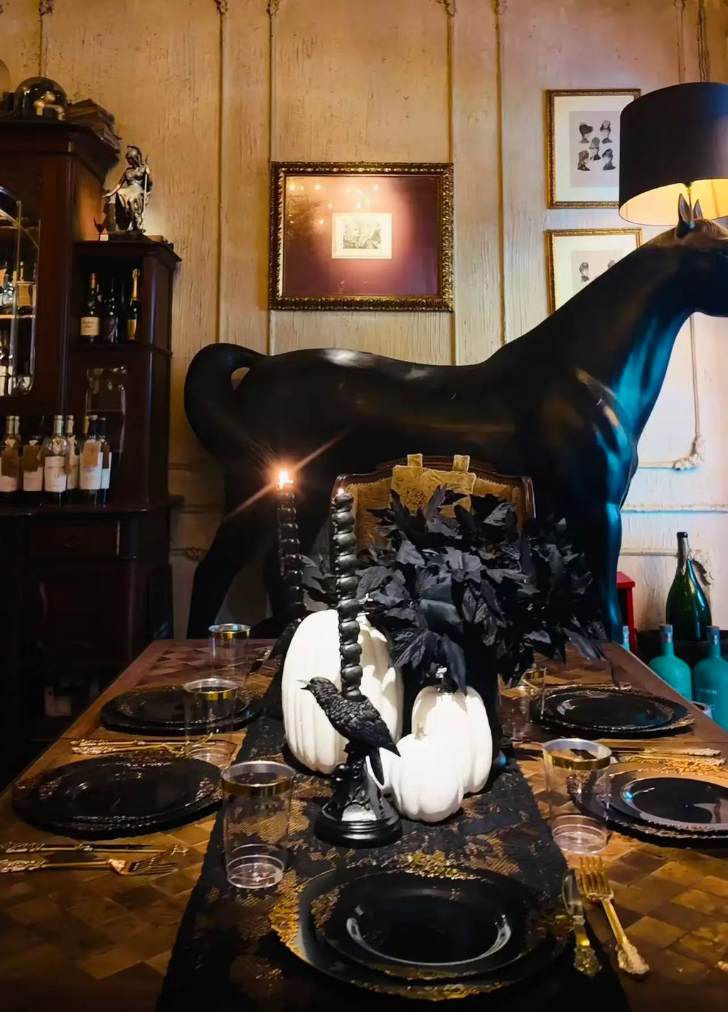 Gothic Halloween dining table scene with black horse statue, white pumpkins, black candles, black lace table runner and gold tableware