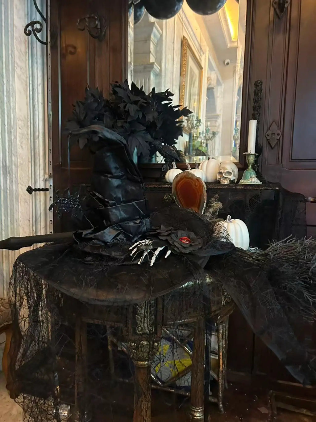 Gothic witch party decor display with black witch hat, broom, white pumpkins, skull, black foliage and dark vintage background