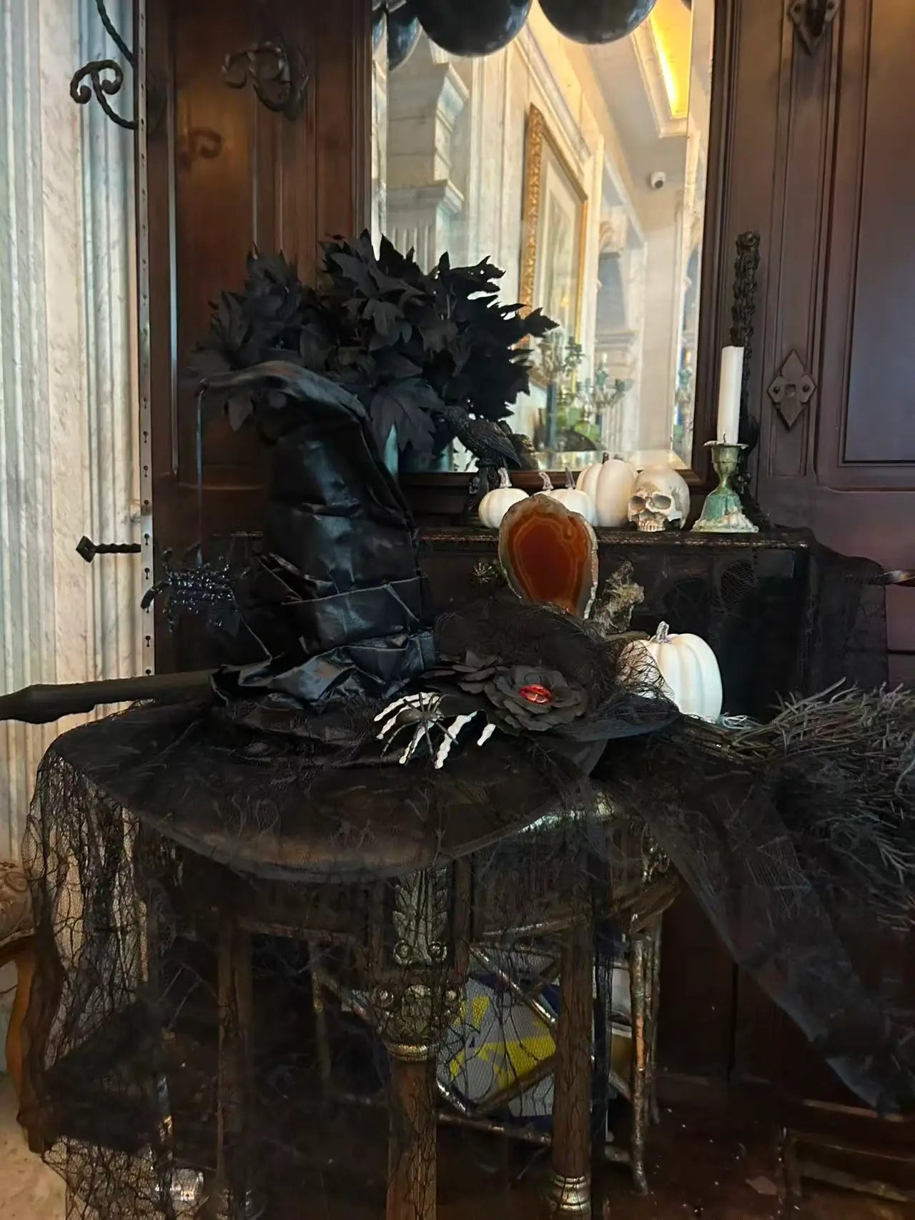 Gothic witch party decor display with black witch hat, broom, white pumpkins, skull, black foliage and dark vintage background